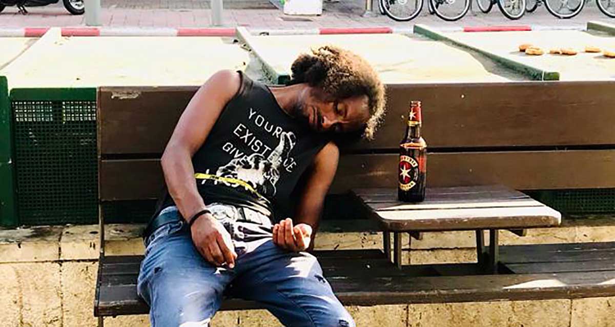דר רחוב נרדם על ספסל ליד בקבוק בירה בדרום תל אביב