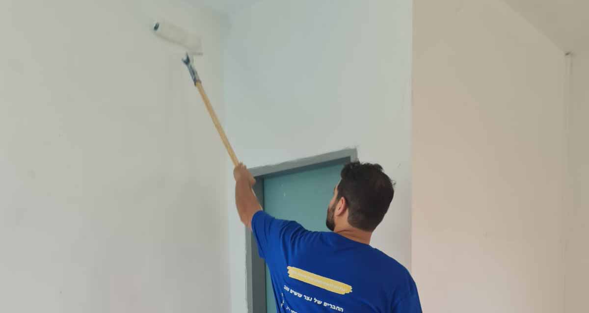 מתנדב חבר של רס"ן (מיל) נצר שמחי ז"ל צובע קירות בפנימייה נווה הדר, הוא לובש חולצה כחולה של קבוצת החברים המתנדבים