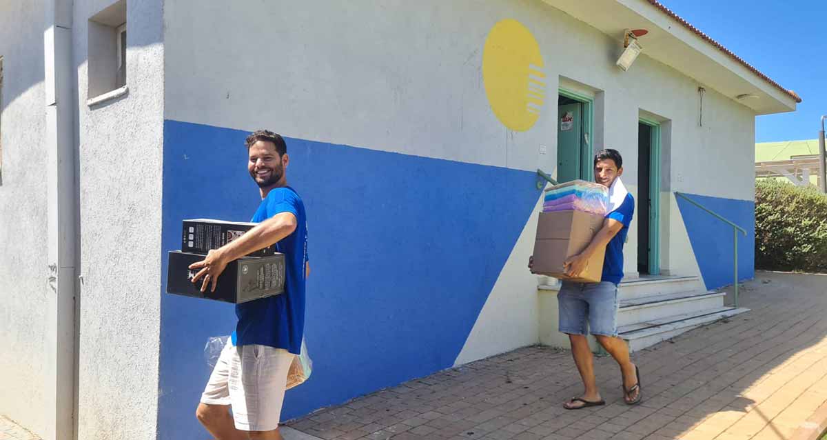 מתנדבים חבריו של רס"ן (מיל) נצר שמחי ז"ל עם ציוד שהביאו לשיפוץ מבנים בפנימיית נווה הדר. החברים נושאים קרטונים ולבושים בחולצות כחולות שהזמינו עבור הקבוצה