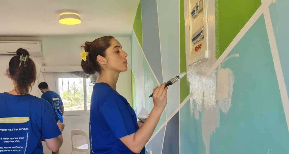קבוצת מתנדבות ומתנדבים חברים של נצר שמחי משפצים מבנים. הקבוצה בחולצות כחולות המיוחדת לקבוצה מתקנת צבע בקירות מבנה