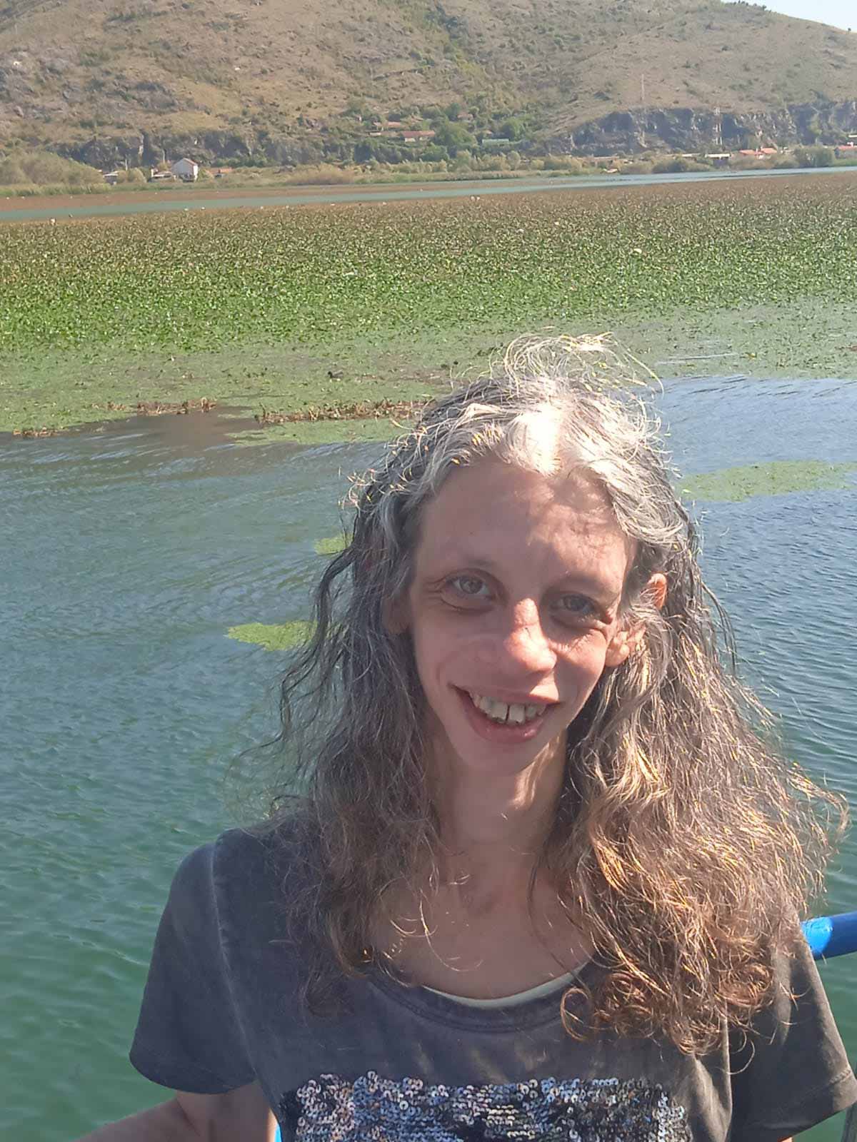 שירה טל עומדת כשברקע נהר עם ירוקת והר ירוק.