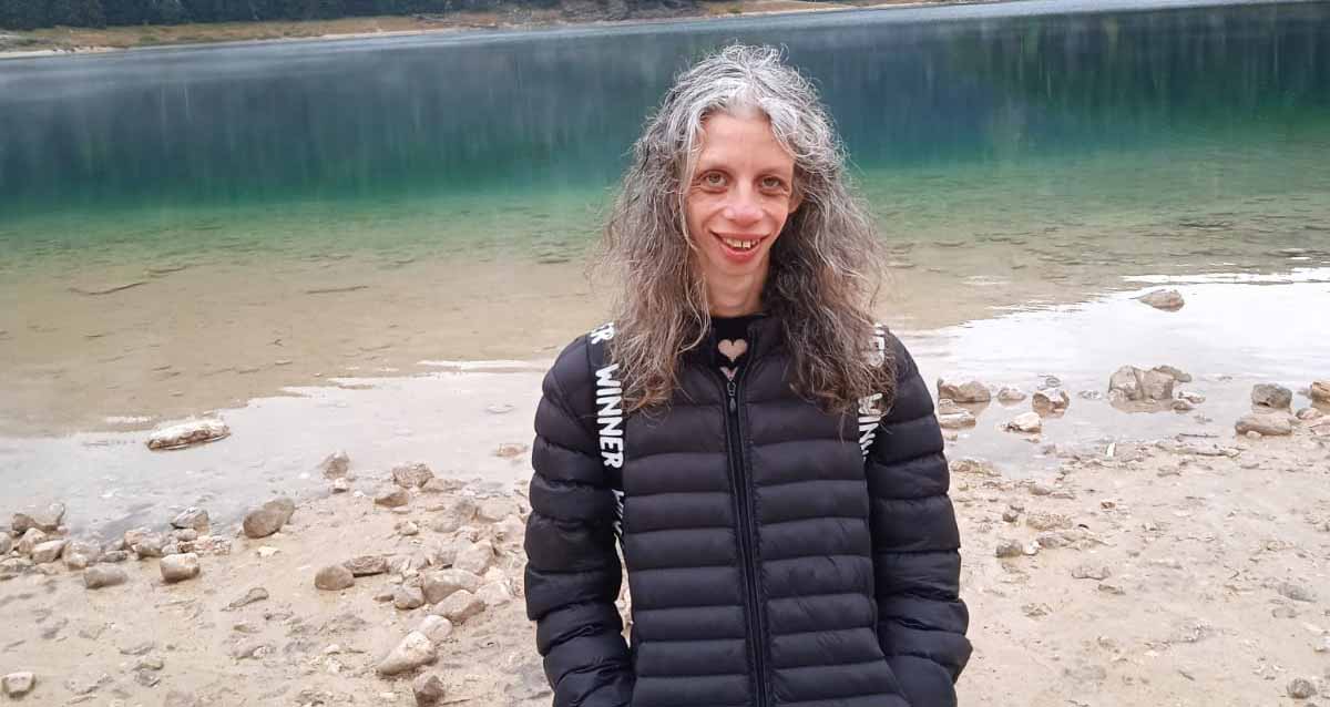 שירה טל עומדת על שפת נהר, לבושה במעיל שחור.