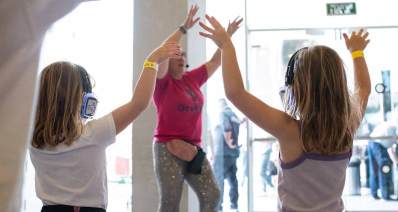 חודש השוויון לזכויות אנשים עם מוגבלויות 2024. אישה ושתי ילדות עם אוזניות וידיים מורמות כלפי מעלה.