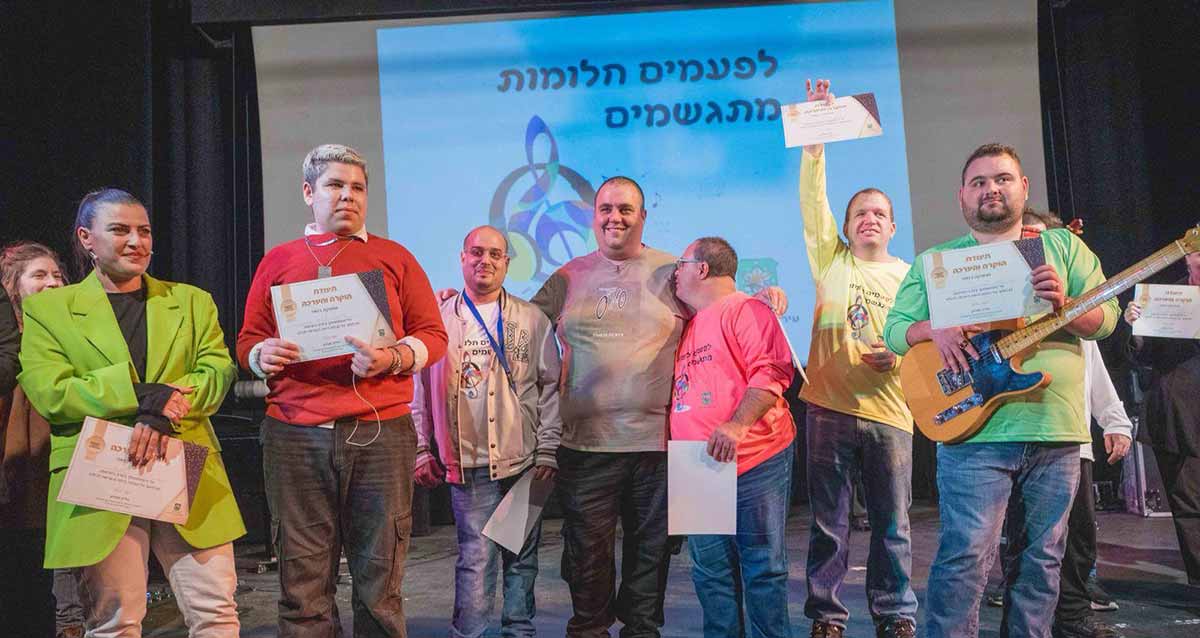 ערב כשרונות לאנשים עם מוגבלות ברמת גן. צילום קבוצתי עומדים בשורה עם תעודות. מאחוריהם מוקרן על מסך הכיתוב: לפעמים חלומות מתגשמים.