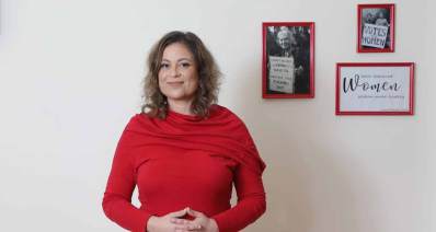 ענבל חרמוני , יו"ר איגוד העובדים הסוציאליים בבגד אדום ומאחוריה על הקיר שלוש תמונות עם כיתובים באנגלית. באחת הכיתוב: Women, בשנייה הכיתוב: VOTES for WOMEN, והשלישית אישה עם פלקט באנגלית.