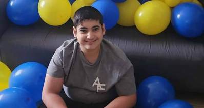 הכשרון המיוחד של שלומי בן 13.5. תמונה של פלג גוף עליון, לבוש בטישרט אפור ועליו באנגלית: AE. סביבו בלונים כחולים וצהובים.