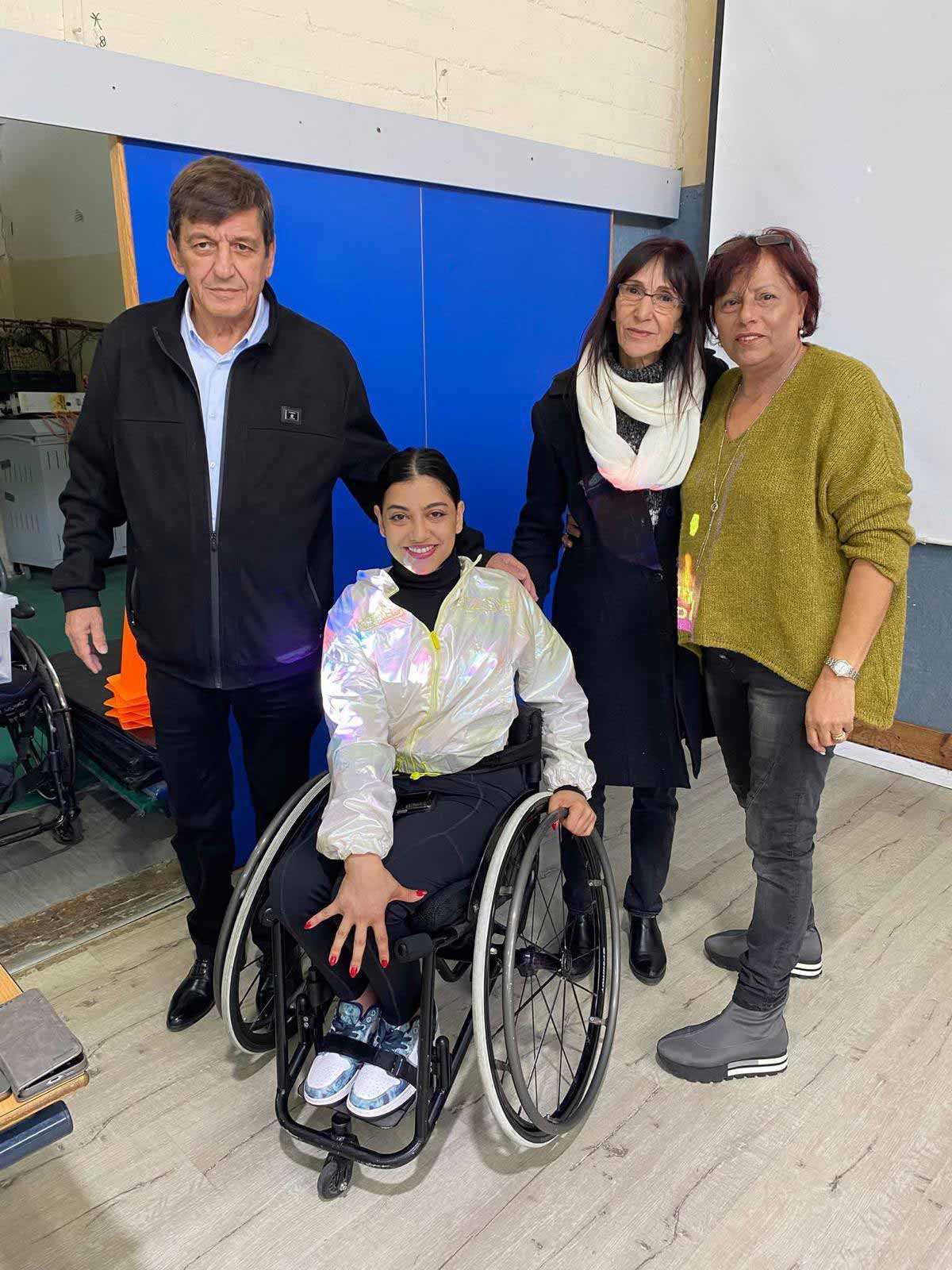 אלופי אירופה בריקוד בכסאות גלגלים עם תלמידי קריית ים. רקדנית על כסא גלגלים ולידה עומדים גבר ושתי נשים.