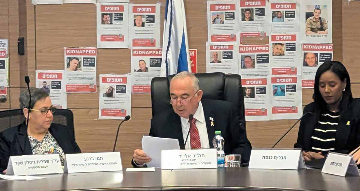 חבר כנסת אלי דלל, הליכוד, יו"ר הוועדה לזכויות הילד. מימינו ומשמאלו יושבות שתי נשים, ומיקרופונים לפניהם. על הקיר מאחוריו תמונות של חטופים וחטופות.