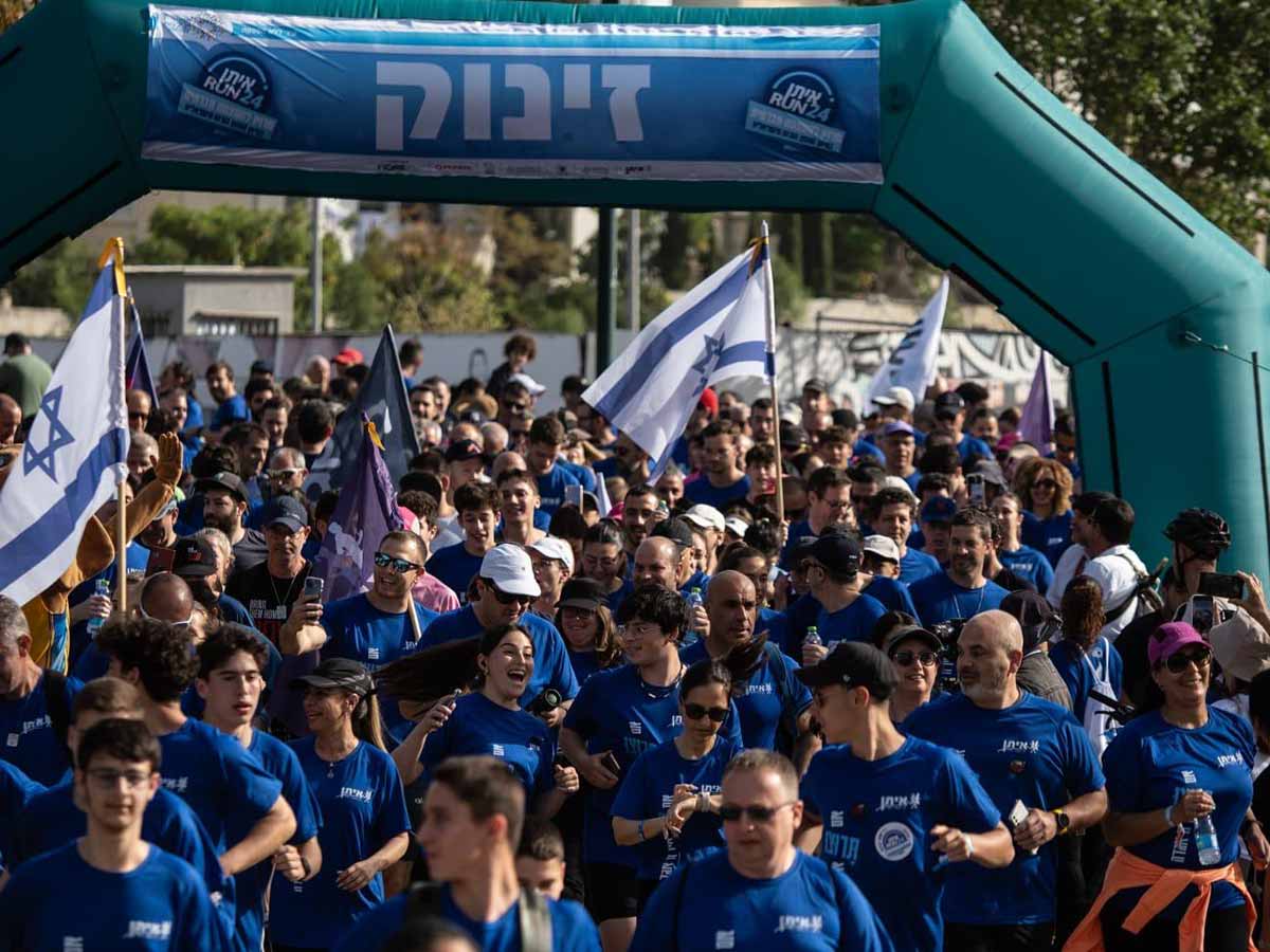 מרוץ איתן RUN. בנקודת הזינוק מתחת לשער עם הכיתוב: זינוק, עומדים המון רצים, בחולצות כחולות וחלקם עם דגלים.