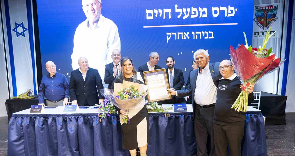 בניהו אחרק מנכ"ל אקים חדרה מקבל פרס מפעל חיים. בניהו עם התעודה ולידו אישה ואיש עם זרים ביד. מאחוריהם שולחן האירוע עם המכובדים עומדים. מאחור על הקיר כיתוב על רקע כחול: פרס מפעל חיים בניהו אחרק ותמונה שלו.