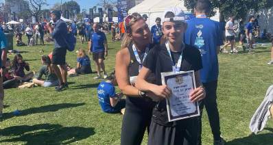 עינבר יצחקי בן 13.5 ואימו מירב במרוץ תל אביב. עינבר עם תעודת הוקרה. ברקע ספורטאים על דשא.