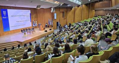 יום העובדות והעובדים הסוציאליים הבין-לאומי. העובדים יושבים באולם ועל הבמה נואם לפני דוכן. על מסך מוקרן הכיתוב: יום העובדות והעובדים הסוציאליים הבין-לאומי, בסימן העובד הסוציאלי כמנהיג שינוי חברתי.