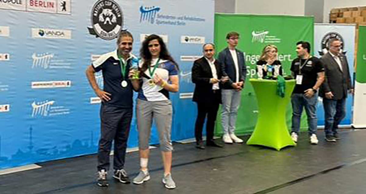 ליהיא בן דוד ורז שוהם, כדורשער ברלין 2025 עם הגביע. מימין דוכן הפרסים וחמישה אנשים משני צידי הדוכן. מאחור על הקיר שלט בד גדול ולמעלה הכיתוב באנגלית: BERLIN. וסמלים על השלט.