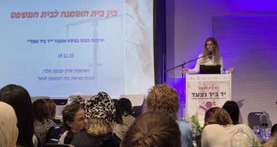 כנס האומנה בכפר המכביה. על במה אישה ליד דוכן נואמים. על הדוכן כיתוב: יום עיון אומנה, יד ביד נצעד. על מסך מוקרן הכיתוב: בין בית האומנה לבית המשפט, הרצאה בכנס בנושא אומנה "יד ביד נצעד", 19.1.25, השופטת שרון עצמון הלוי, סגנית נשיאת בתי המשפט לנוער.